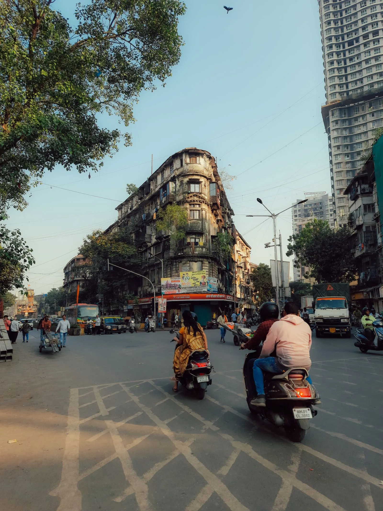 Riders and scooters moving through an Indian city street at dusk.