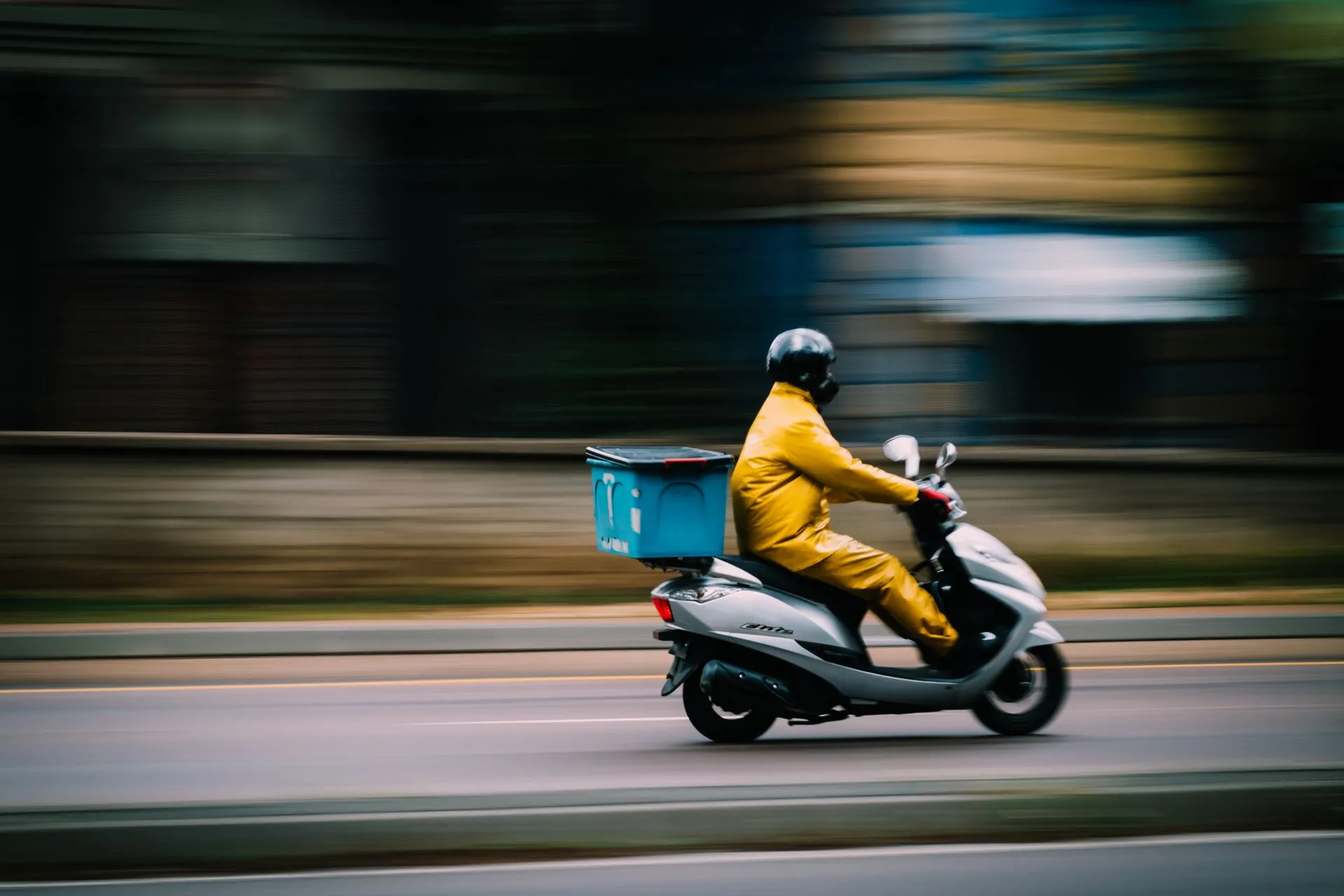 A delivery rider moving through the city on a scooter with an insulated delivery box.