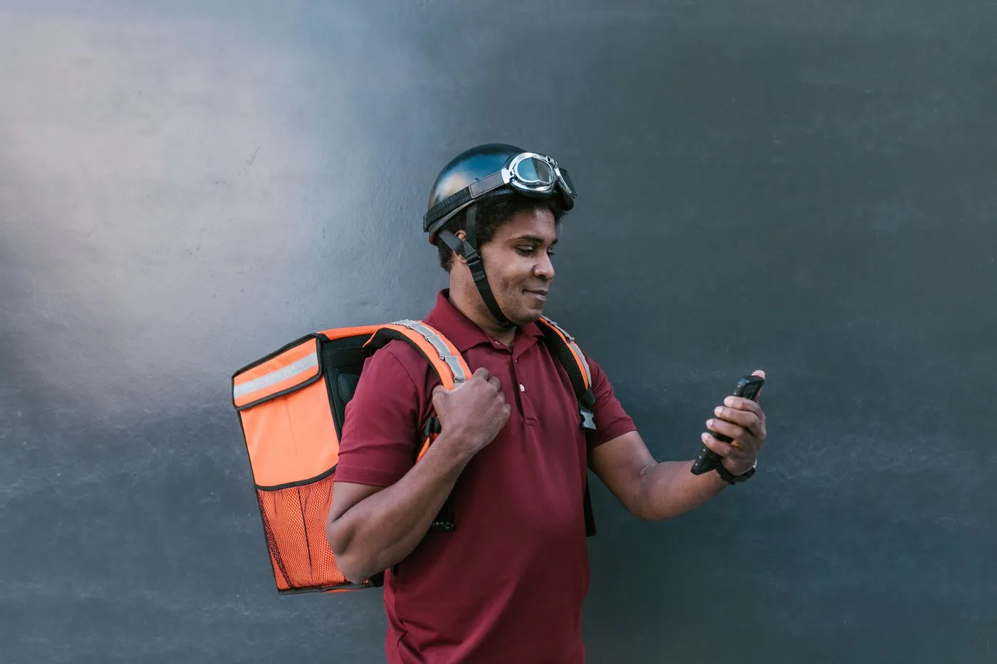 A delivery rider with a helmet and insulated backpack, phone in hand.
